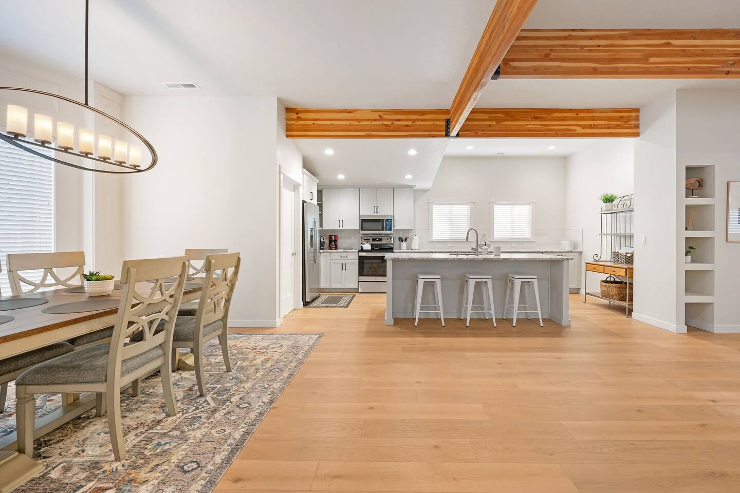 Dining table under exposed wood beams, open to the kitchen