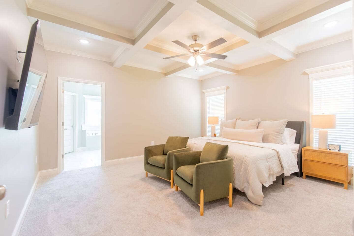 Primary bedroom with king bed, two armchairs and wall-mounted smart TV