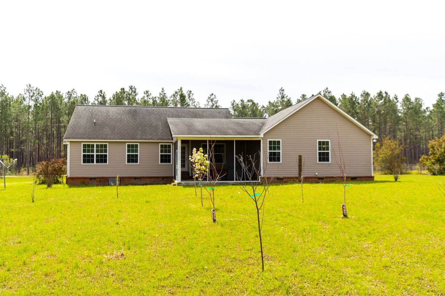 Back of the home with screened porch, wide lawn and tall pines