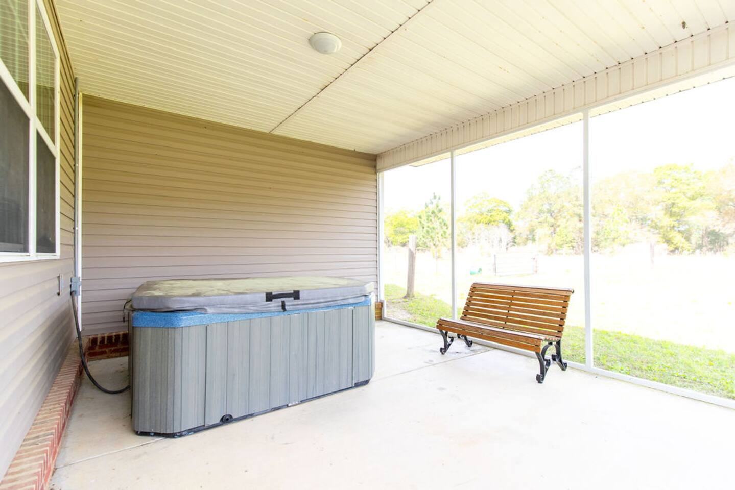 Screened porch with hot tub and bench looking out to the yard