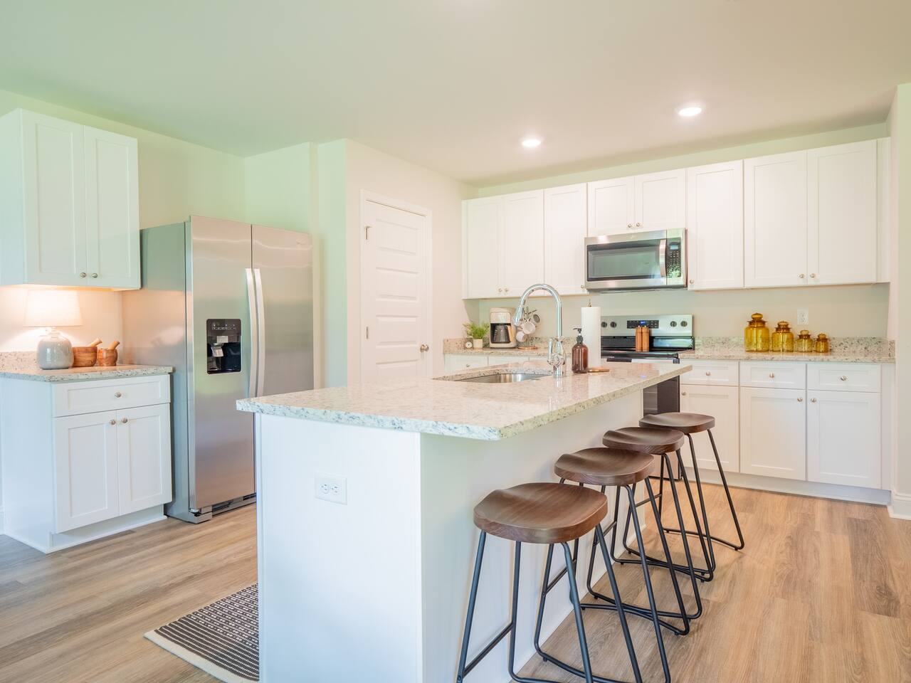 Kitchen with white shaker cabinets, a granite island with bar stools and stainless appliances